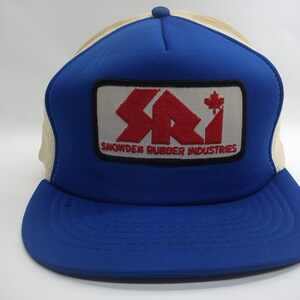 May include: A blue and white trucker hat with a red, white, and black patch that says "SRI Snowden Rubber Industries" with a Canadian maple leaf.