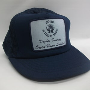 Puede incluir: Una gorra de camionero azul marino con un parche blanco que dice "1947-1987 40 años de servicio Dryden District Credit Union Limited".