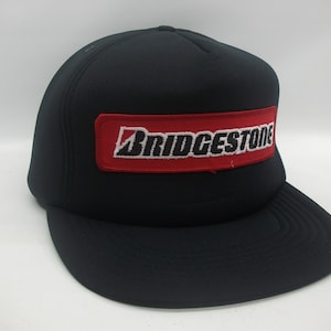 May include: A black trucker hat with a red and white embroidered patch that says "BRIDGESTONE".