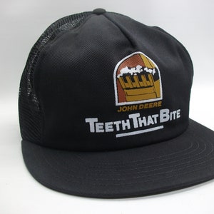May include: Black mesh trucker hat with a John Deere logo and the text "Teeth That Bite".