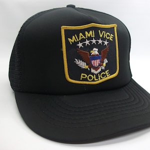 May include: Black trucker hat with a yellow embroidered patch that says "Miami Vice Police" with an eagle and stars.