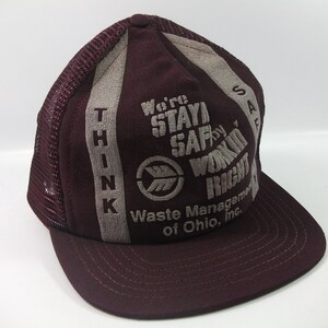 May include: A burgundy and gray trucker hat with the text "Think" on the left side and "We're Stayin' Safe by Workin' Right Waste Management of Ohio, Inc." on the right side.
