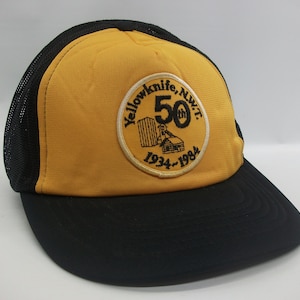 Peut inclure: Casquette de camionneur jaune et noire avec un écusson brodé noir qui dit "Yellowknife, N.W.T. 50th 1934-1984".