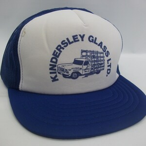 May include: A white and blue trucker hat with the text "Kindersley Glass LTD." and a graphic of a truck carrying glass panels.