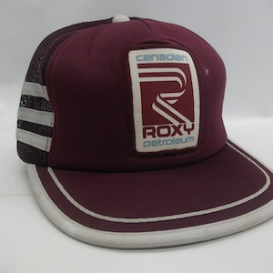 May include: A maroon trucker hat with a white mesh back and a white stripe. The front of the hat has a white patch with the text "Canadian Roxy Petroleum" and a stylized "R" logo.