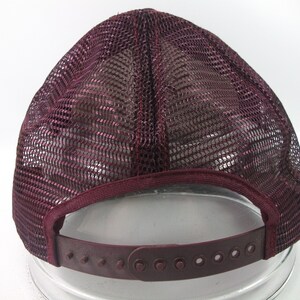 May include: A burgundy mesh trucker hat with a plastic adjustable strap in the back.