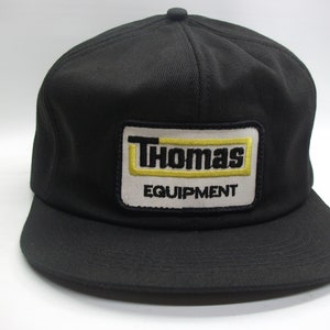 May include: Black trucker hat with a white and yellow patch that says "Thomas Equipment"