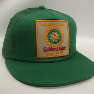 May include: Green trucker hat with a yellow and white patch featuring the Moosehead's Golden Light beer logo. The patch has the text "Moosehead's 1912 1978 Golden Light Beer Biere".