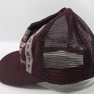May include: A maroon and grey mesh trucker hat with the words "Safety First" printed on the front.