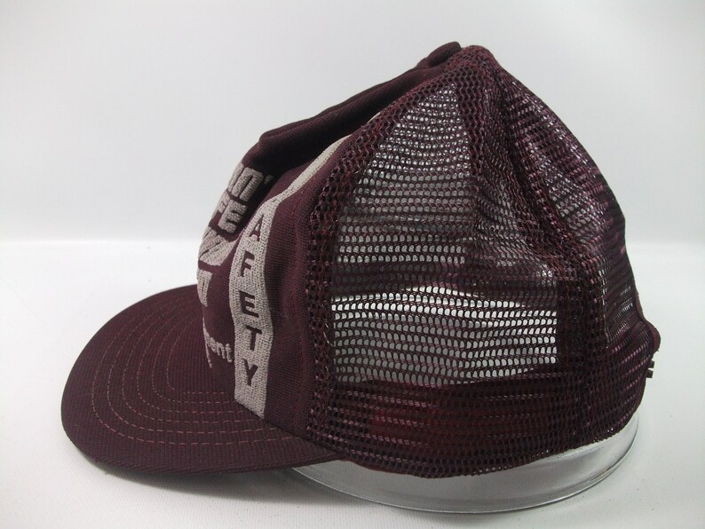 May include: A maroon and grey mesh trucker hat with the words "Safety First" printed on the front.