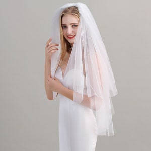 May include: A white bridal veil with a single layer of tulle. The veil is gathered at the top and falls to the shoulders.