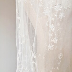 Pu&ograve; includere: Un velo da sposa bianco con delicati ricami floreali e perline. Il velo &egrave; realizzato in tessuto morbido e trasparente, perfetto per una cerimonia di matrimonio.