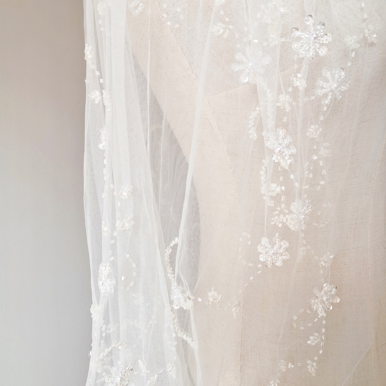 Pu&ograve; includere: Un velo da sposa bianco con delicati ricami floreali e perline. Il velo &egrave; realizzato in tessuto morbido e trasparente, perfetto per una cerimonia di matrimonio.