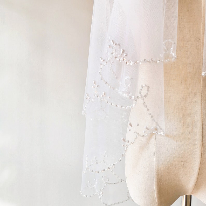 May include: A white bridal veil with a beaded trim. The veil is made of soft tulle and has a delicate, feminine look.