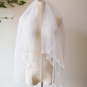 May include: A white bridal veil with a delicate beaded trim. The veil is layered and has a scalloped edge.