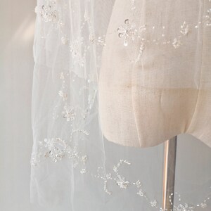 Pu&ograve; includere: Un velo da sposa bianco con ricami floreali delicati e decorazioni scintillanti. Il velo &egrave; realizzato in tulle morbido ed &egrave; perfetto per una cerimonia di matrimonio.