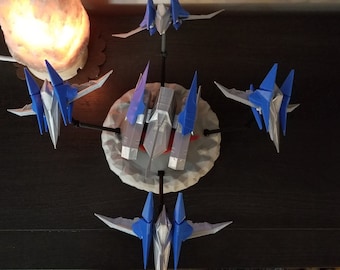 May include: A collection of six blue and silver model spaceships on a gray and white base. The spaceships are arranged in a circle around the base, with the center spaceship facing forward.