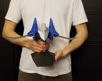 May include: A 3D-printed model of a spacecraft, featuring a silver and blue color scheme. The model has wings and is mounted on a black base. The spacecraft is held in front of a person wearing a white t-shirt.