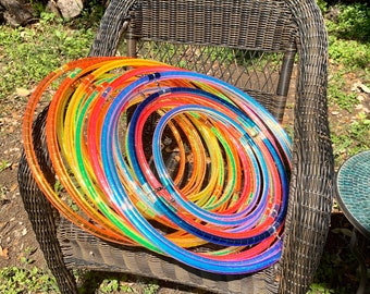 May include: A stack of colorful plastic hula hoops in various sizes, arranged in a rainbow pattern, sitting on a wicker chair.