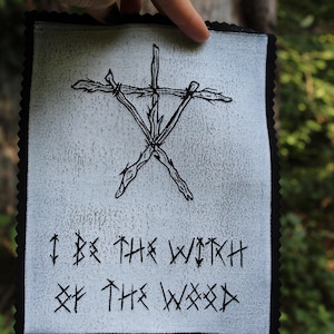 May include: Black and white embroidered patch featuring a stylised symbol of a five-pointed star made from branches. The text "I BE THE WITCH OF THE WOOD" is written below the symbol in a stylised font.
