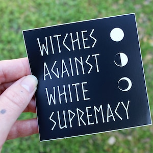 May include: Black and white sticker with the text "Witches Against White Supremacy" and three white moon phases.