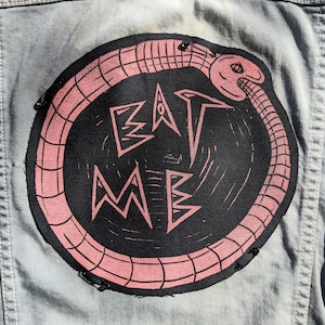 May include: A pink and black embroidered patch with a snake biting its tail around the words "EAT ME".
