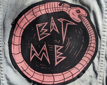 May include: A pink and black embroidered patch with a snake biting its tail around the words "EAT ME".