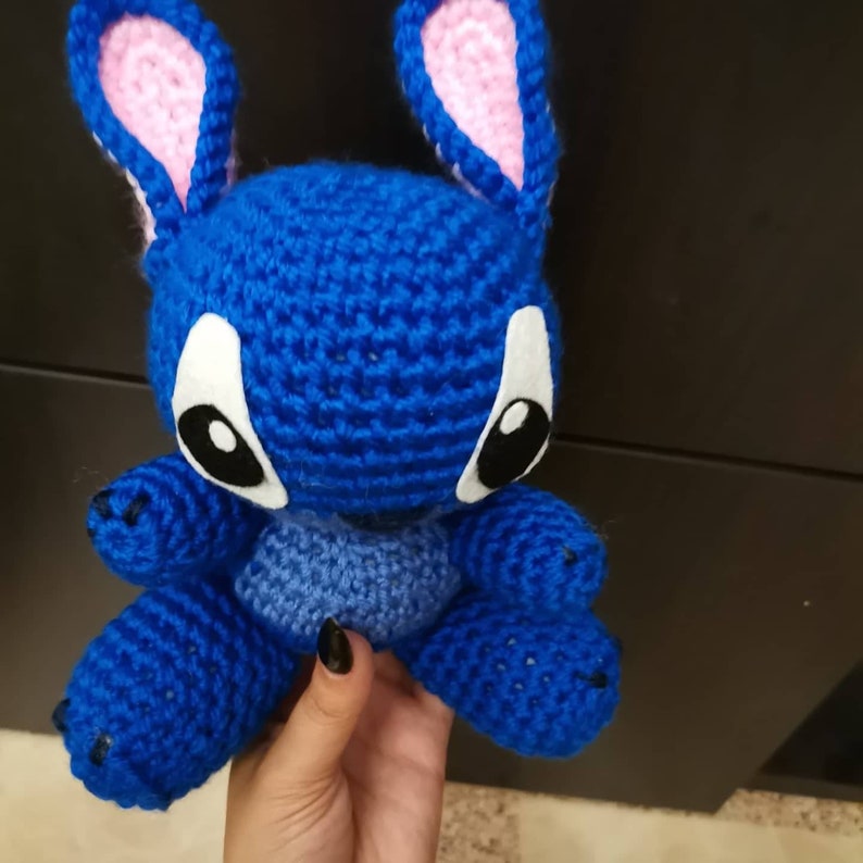 Puede incluir: Peluche de Stitch de color azul tejido a crochet con orejas rosas y ojos negros.