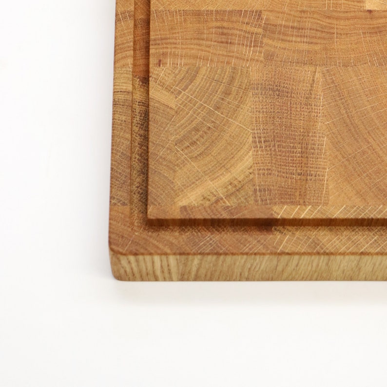 Op de afbeelding: Een close-up van de rand van een houten snijplank. De plank is gemaakt van lichtbruin hout en heeft een natuurlijke houtnerf. De plank is dik en stevig, met een verhoogde rand rondom de omtrek.