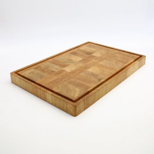 Op de afbeelding: Een rechthoekig houten snijplank met een verhoogde rand en een geruit patroon. De plank is gemaakt van lichtbruin hout en heeft een natuurlijke afwerking.