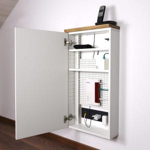 Puede incluir: Armario blanco con una puerta de espejo, abierto para revelar estantes con un router, un modem y otros dispositivos electrónicos. El armario tiene una tapa de madera y un respaldo de tablero perforado.