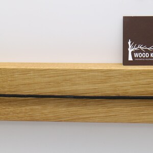 May include: A wooden shelf with a black cord running across the front. A brown business card with the text "WOOD KOPF" is placed on the shelf.