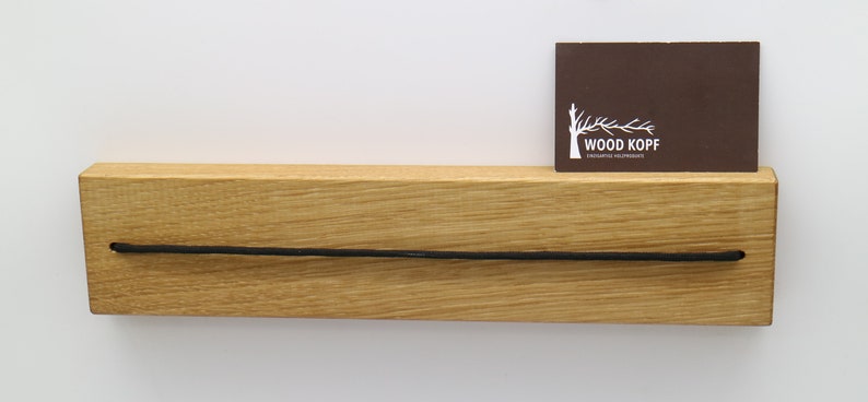 May include: A wooden shelf with a black cord running across the front. A brown business card with the text "WOOD KOPF" is placed on the shelf.