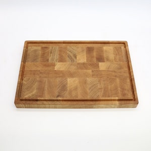 Op de afbeelding: Een groot, rechthoekig houten snijplank met een natuurlijke houtkleur. De plank is gemaakt van meerdere stukken hout die aan elkaar zijn gelijmd om een moza&iuml;ekpatroon te cre&euml;ren.
