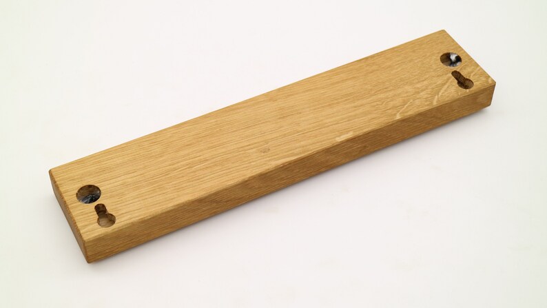 May include: A wooden wall mount with two holes for hanging. The mount is made of light brown wood and has a smooth finish.