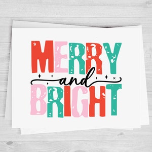May include: A white card with the text "Merry and Bright" in colorful, distressed lettering. The letters are in shades of red, pink, green, and teal.