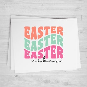 Pu&ograve; includere: Un biglietto bianco con il testo "Easter Easter Easter vibes" in lettere rosa, verde e arancio.