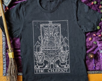 Könnte beinhalten: Schwarzes T-Shirt mit einer weißen Illustration der Wagenkarte aus dem Tarot-Deck. Die Karte zeigt eine Figur in einem Wagen, der von zwei Sphinxen gezogen wird. Der Text "VII THE CHARIOT" ist unter dem Bild gedruckt.