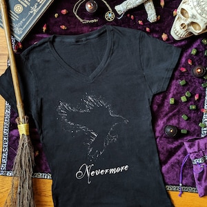 May include: Black v-neck t-shirt with a white silhouette of a raven and the text "Nevermore" printed on the front.