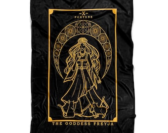 Può includere: Una coperta in pile nero con un'illustrazione dorata di una donna con i capelli lunghi e una corona, in piedi con due gatti. L'illustrazione è circondata da un cerchio di lune e stelle. Il testo "~X~ FORTUNE THE GODDESS FREYJA" è stampato sotto l'illustrazione.
