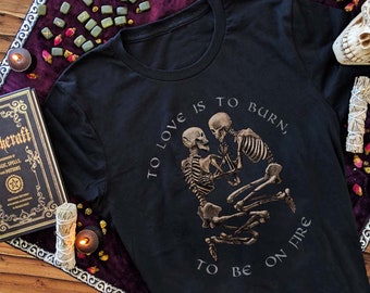 May include: Black t-shirt with a graphic of two skeletons embracing. The text "To love is to burn, to be on fire" is printed on the shirt.