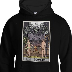 Puede incluir: Sudadera con capucha negra con un estampado gr&aacute;fico de una carta del tarot que representa a Los Amantes. La carta muestra una figura esquel&eacute;tica con los brazos extendidos, dos figuras desnudas y el texto "THE LOVERS" en la parte inferior.
