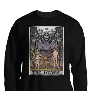 Puede incluir: Sudadera negra con un gr&aacute;fico de la carta del tarot de Los Amantes. La carta presenta una figura esquel&eacute;tica con alas extendidas, dos figuras desnudas y un volc&aacute;n. El texto "THE LOVERS." est&aacute; impreso debajo de la carta.