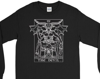 Pode incluir: Camiseta preta de manga comprida com uma ilustração branca do cartão do Diabo de um baralho de tarô. O cartão apresenta uma figura com chifres, asas e um pentagrama. O texto "THE DEVIL." está impresso abaixo da imagem.