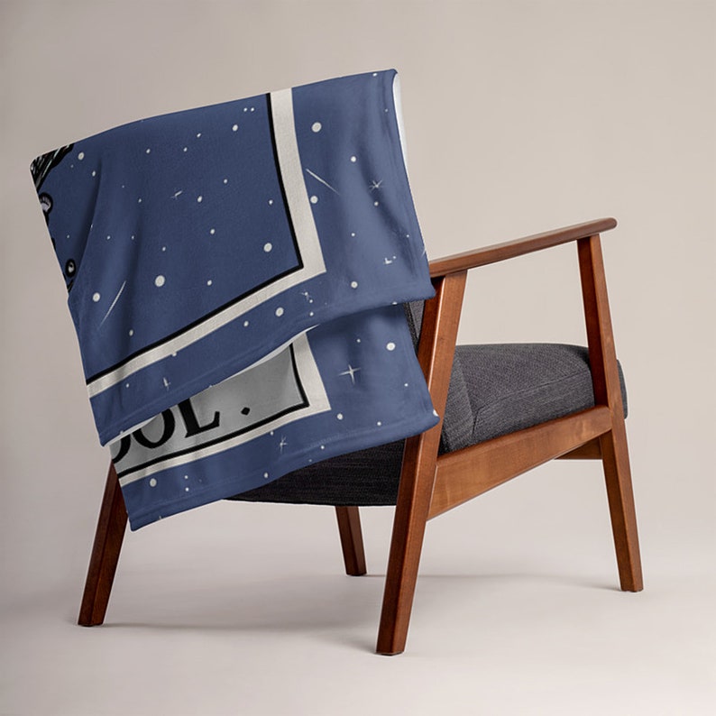 May include: A blue throw blanket with a white border and a star pattern. The blanket is folded and draped over a wooden chair. The text "COOL." is visible on the blanket.