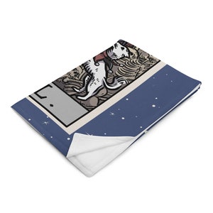 May include: A blue and white throw blanket with a tarot card design featuring a white dog with a red collar. The card is surrounded by a blue background with white stars.