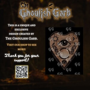 Puede incluir: Dise&ntilde;o de tabla Ouija en forma de coraz&oacute;n con un ojo, sol, luna y otros s&iacute;mbolos en tonos marr&oacute;n y beige sobre fondo negro. El texto incluye "The Ghoulish Garb" e informaci&oacute;n de la tienda.