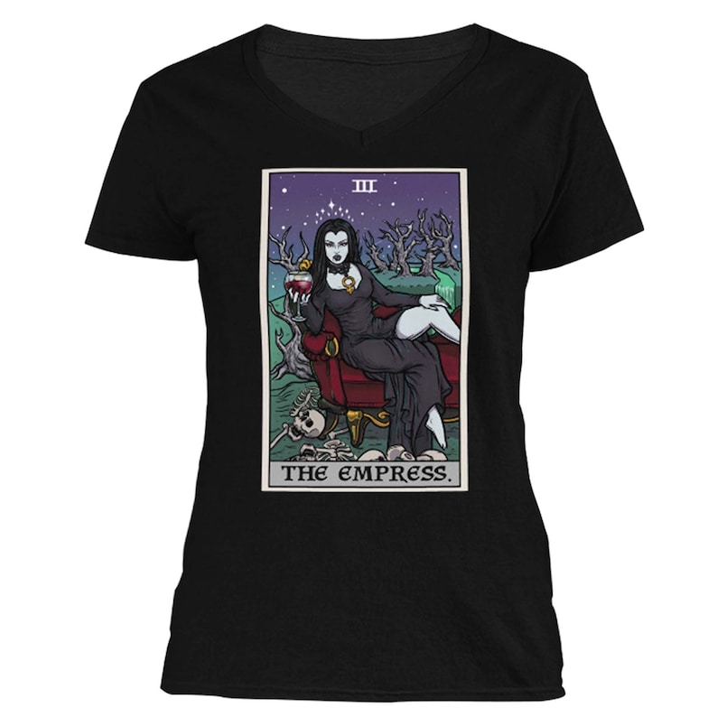 May include: A black v-neck t-shirt with a tarot card illustration of The Empress. The card features a woman sitting on a throne, holding a glass of wine. The card is surrounded by a dark green background with stars and trees.