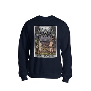 Puede incluir: Sudadera azul marino con un gr&aacute;fico de la carta del tarot de Los Amantes. La carta presenta una figura esquel&eacute;tica con los brazos extendidos, dos figuras de pie a cada lado de un volc&aacute;n, y el texto "THE LOVERS."