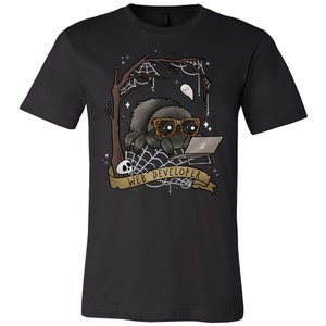 May include: Black t-shirt featuring a cartoon spider wearing glasses and working on a laptop. The design includes a tree, spiderwebs, a ghost, and a banner that reads "WEB DEVELOPER". A skull is also present in the design.
